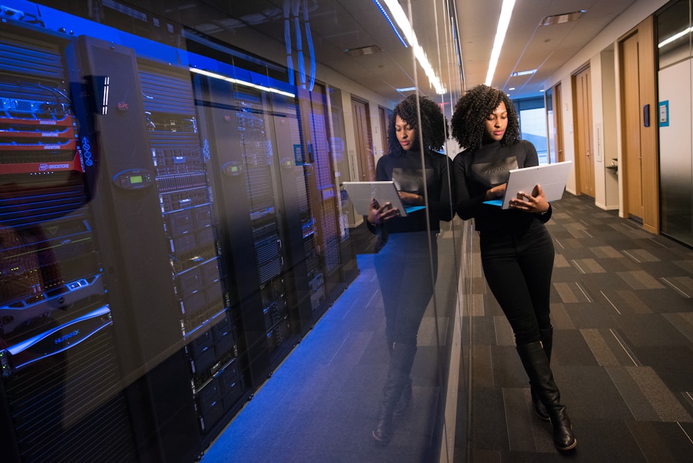 IT engineer walking through a server room aisle reviewing infrastructure status on a tablet